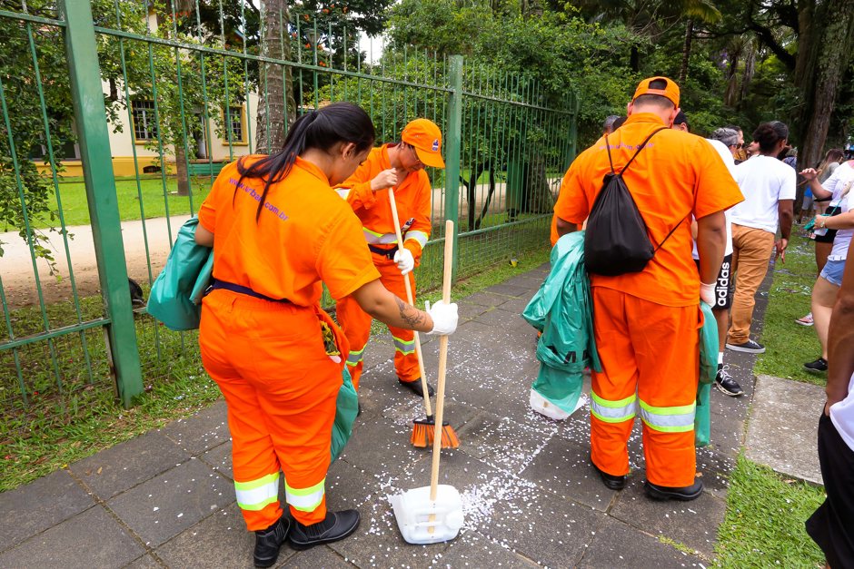 Três trabalhadores da Urbam varrem confetes do chão durante folia em frente ao Parque Vicentina Aranha
