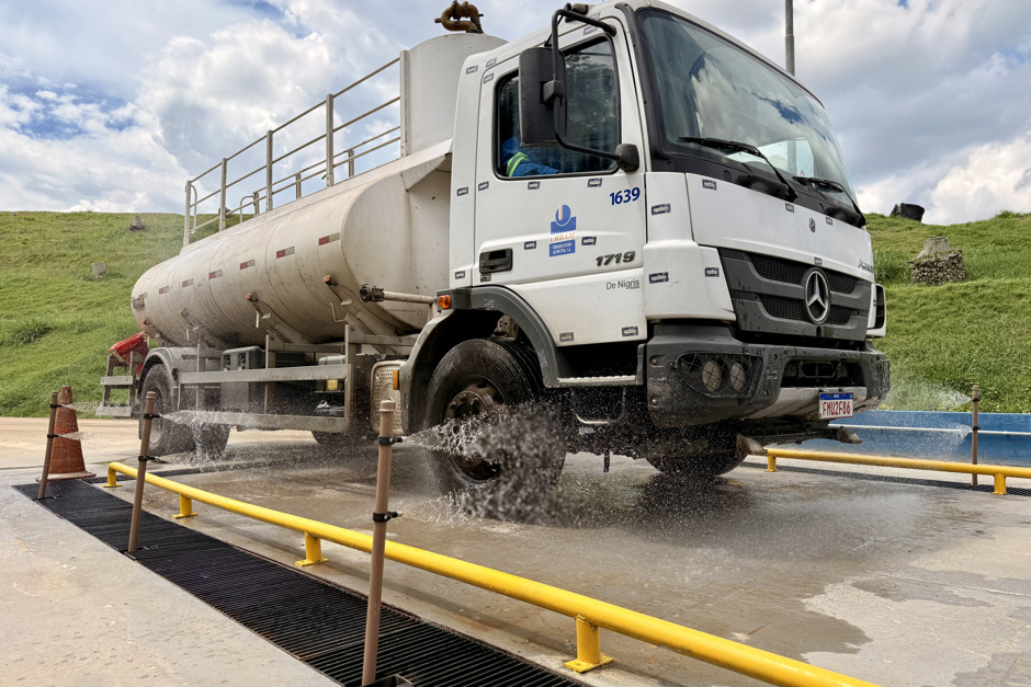 Caminhão da Urbanizadora Municipal passa pela plataforma do lava-rodas que ativa jatos de água para realizar a lavagem do veículo.